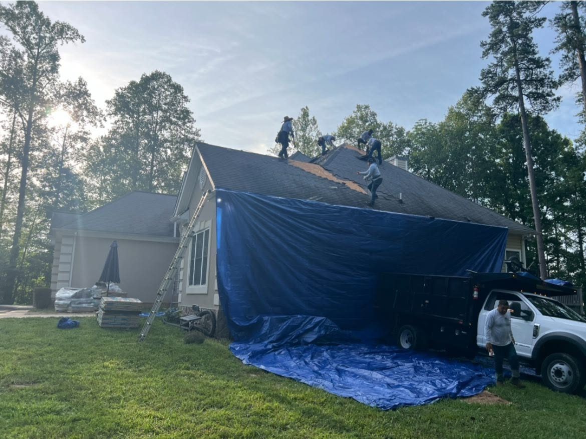 Crew re-roofing a house in Mineral with a tarp protecting the lower roof
